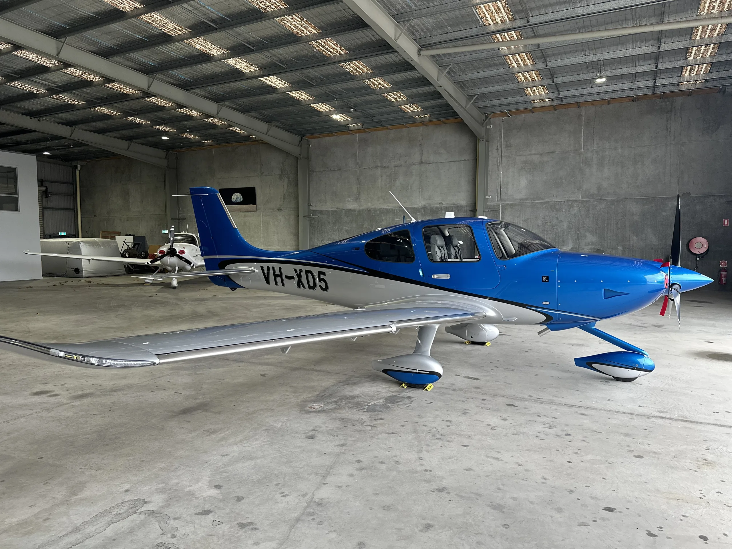 A blue and white single-engine Cirrus SR22 aircraft with registration VH-XD5 parked inside a hangar.