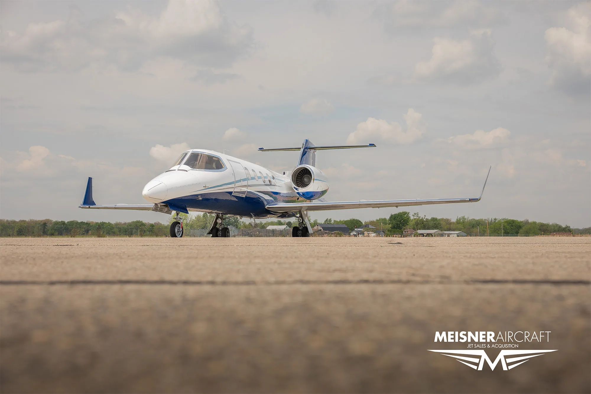A low-angle view of a white and blue Learjet N616LK parked on an airfield.