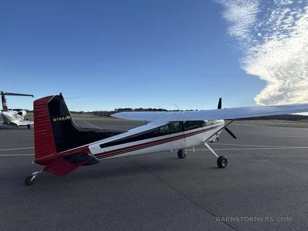 A white and black single-engine propeller aircraft with red accents on the tail, parked on an asphalt tarmac under a blue sky.