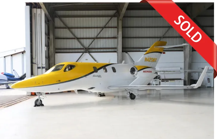 A yellow and white HondaJet (N42QMX) is parked inside a hangar.