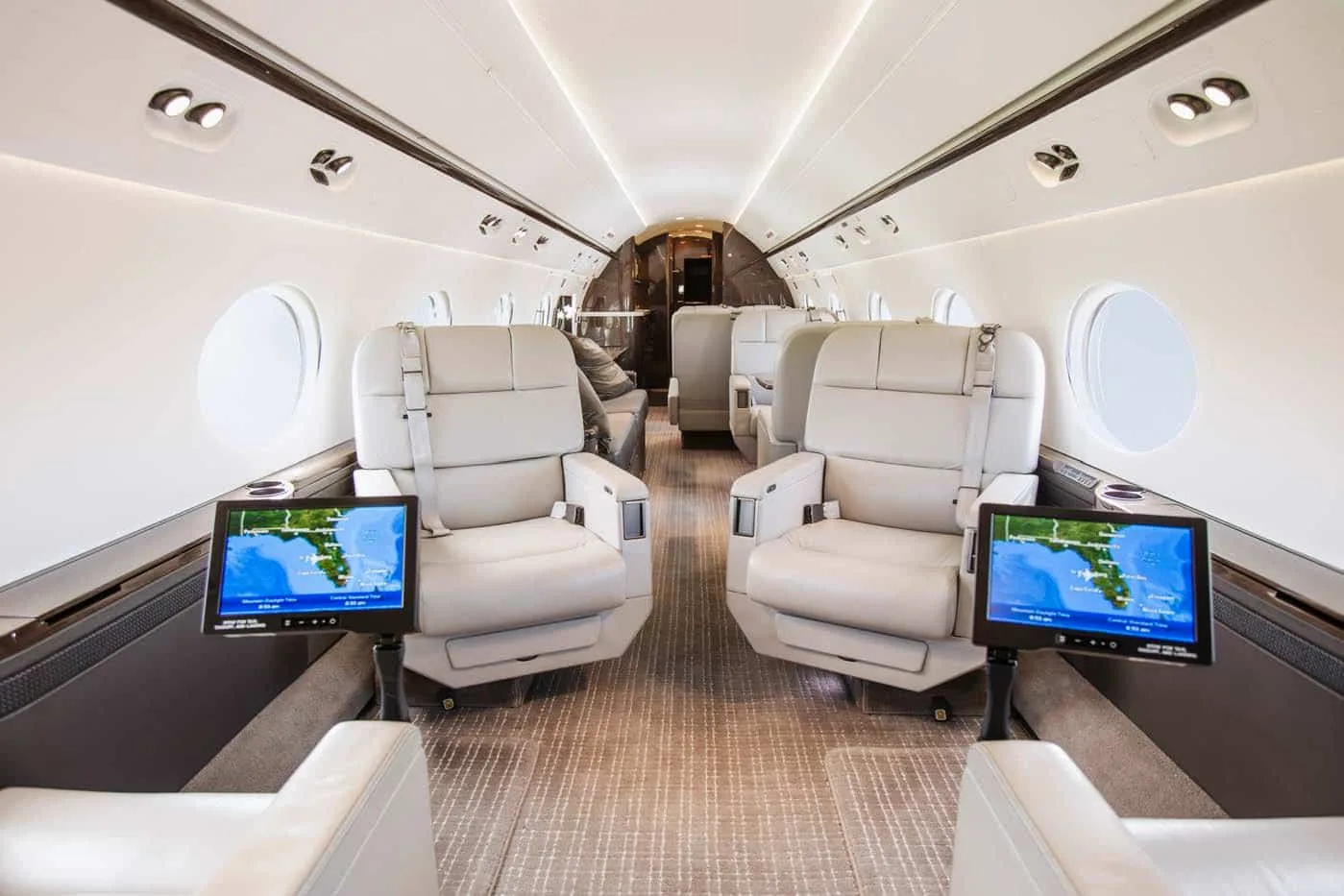 A spacious aircraft cabin with light-colored leather seats and screens showing a map display.