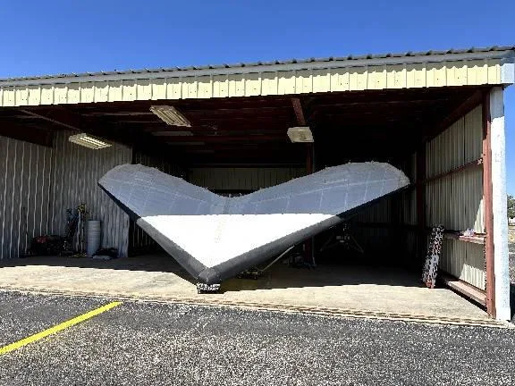 A white and black delta-wing aircraft is stored inside an open hangar.