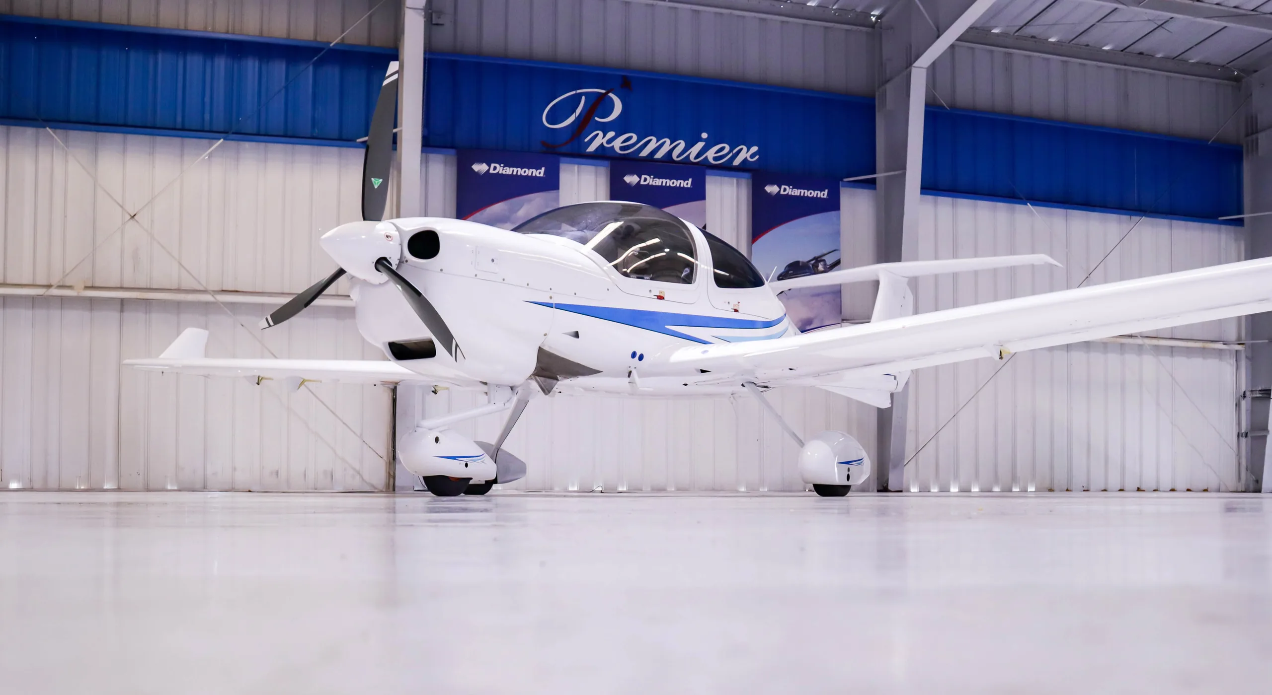 A low-angle view of a white Diamond DA40 aircraft with blue stripes parked inside a hangar.