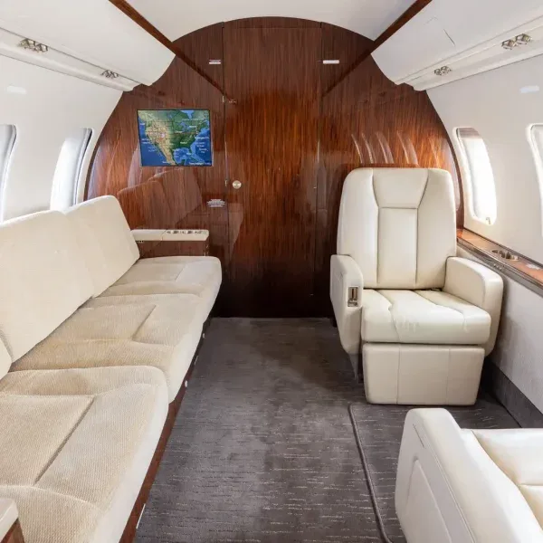 Interior view of a private jet cabin featuring a cream-colored sofa and a single seat, with a map display on the bulkhead.