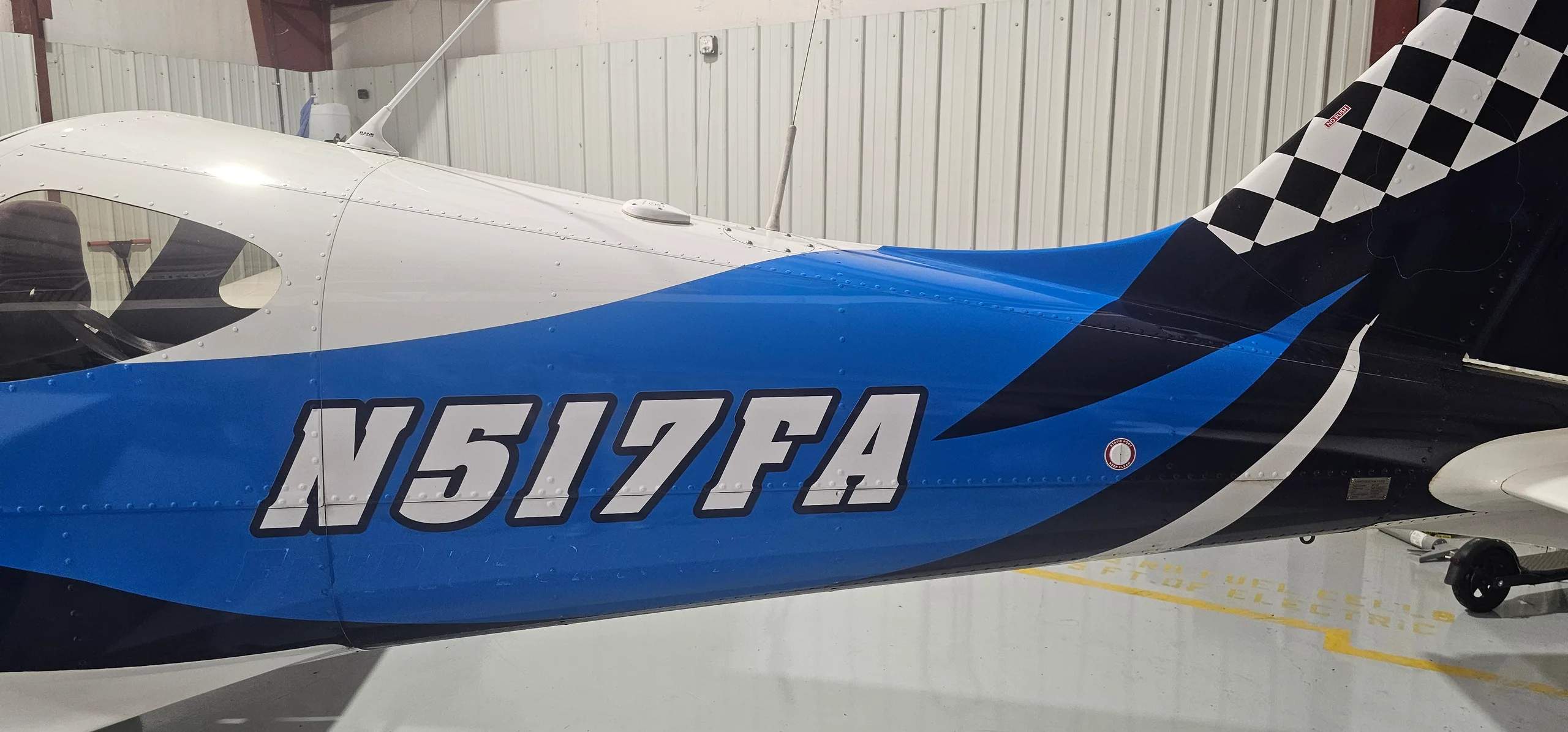 A close-up of the fuselage of a white and blue aircraft, showing the registration N517FA and a checkered tail pattern.
