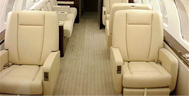 A view down the aisle of an aircraft cabin showing multiple rows of plush beige leather seats.