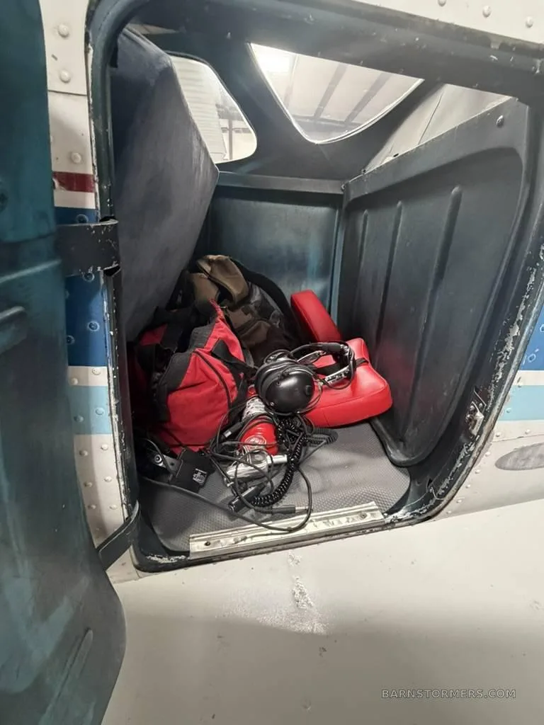 The baggage compartment of a Cessna 172, filled with a red bag, headsets, and other gear.