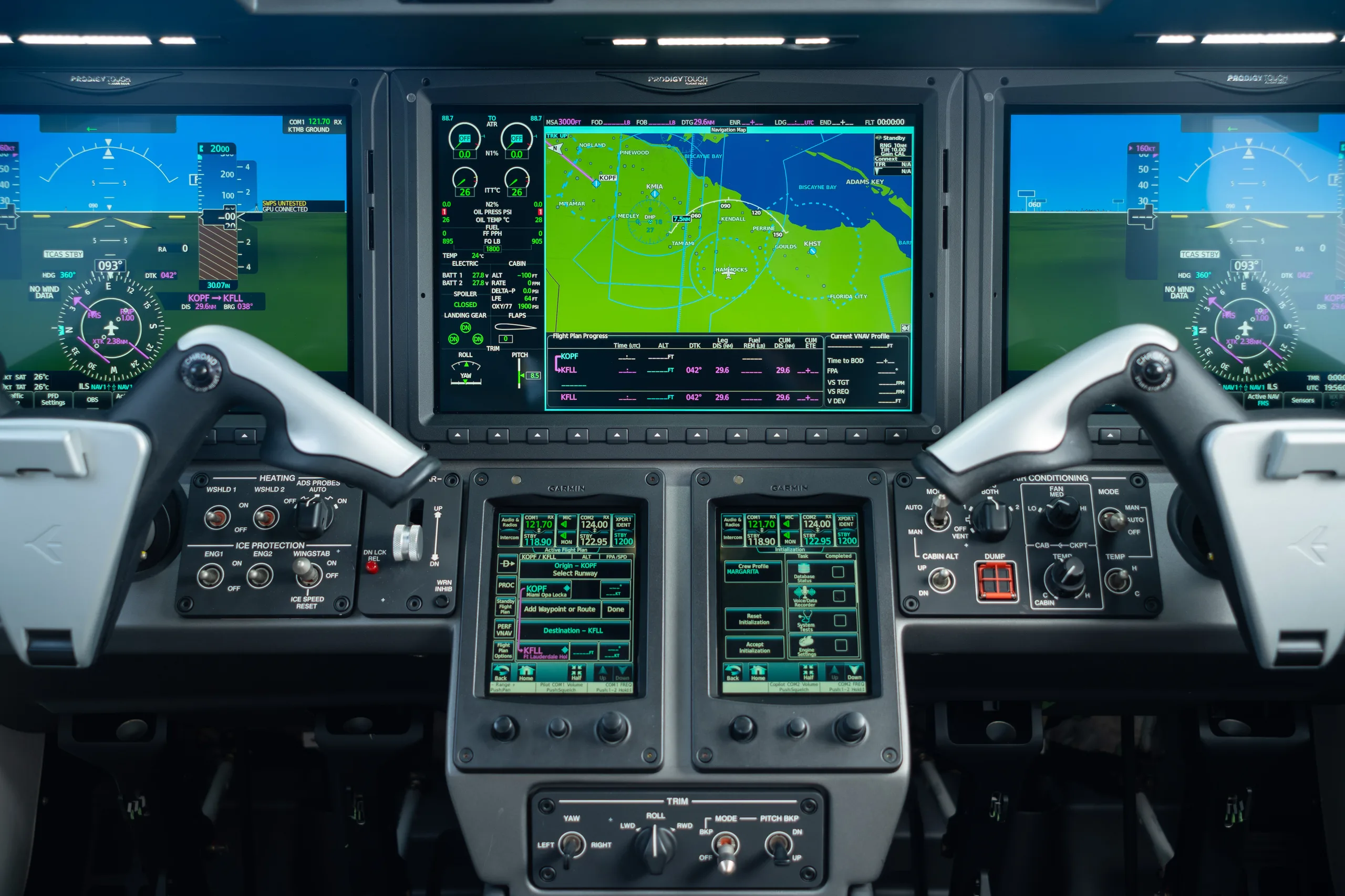 A wide view of the aircraft cockpit showing the main instrument panel with three large digital display screens and various controls.