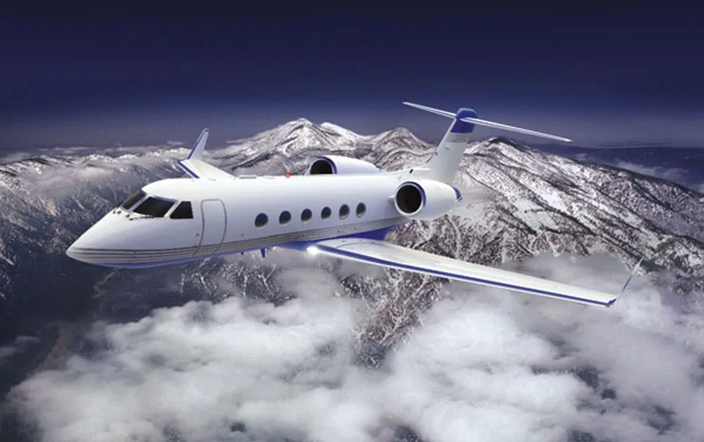 A white business jet with blue accents flies above snow-capped mountains and clouds.
