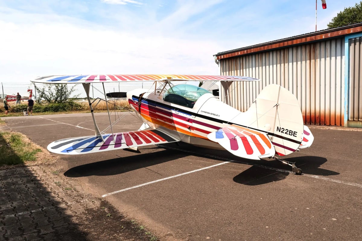 Christen Eagle II biplane with colorful paint scheme parked on the tarmac, side view.