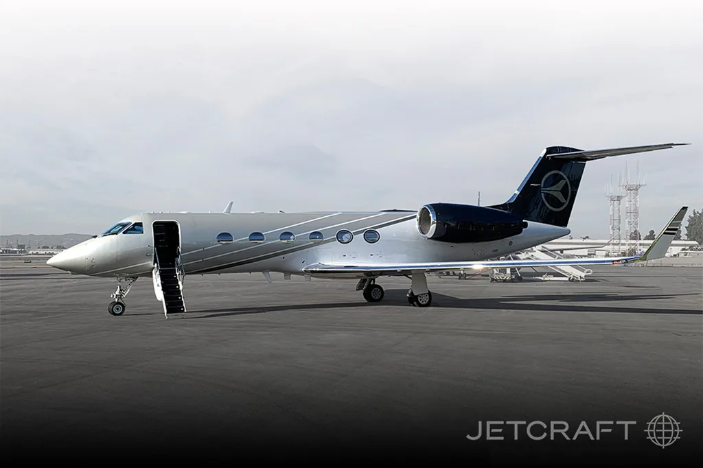 A silver and dark blue Gulfstream G650 private jet with its door open and stairs extended, parked on an airfield.