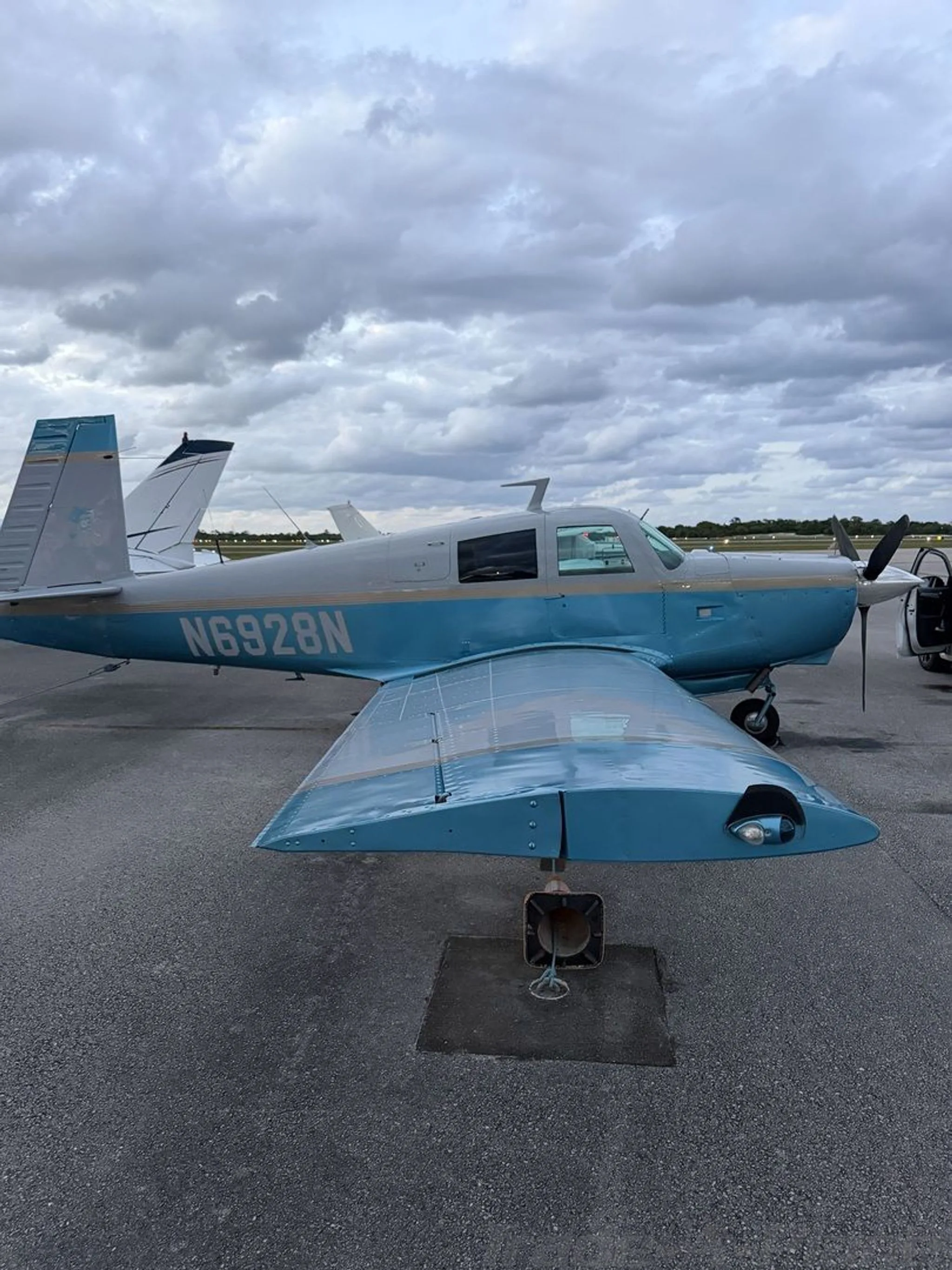 A close-up side view of a light blue and white single-engine aircraft, N6928N, parked on an airport tarmac.