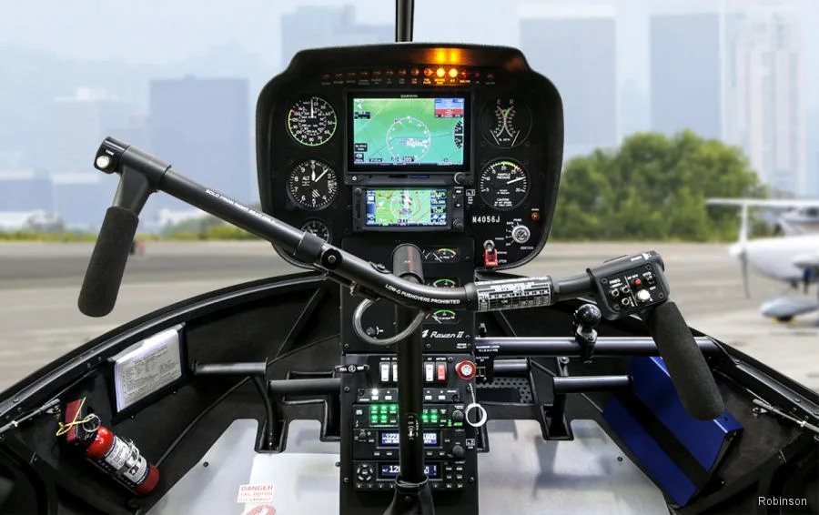 The cockpit of a Robinson R44 helicopter showing the instrument panel, cyclic, and collective controls.