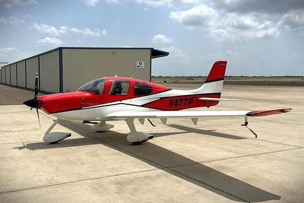 A red and white Cirrus SR22 aircraft, registration N47TP, parked on an airport apron next to a hangar.