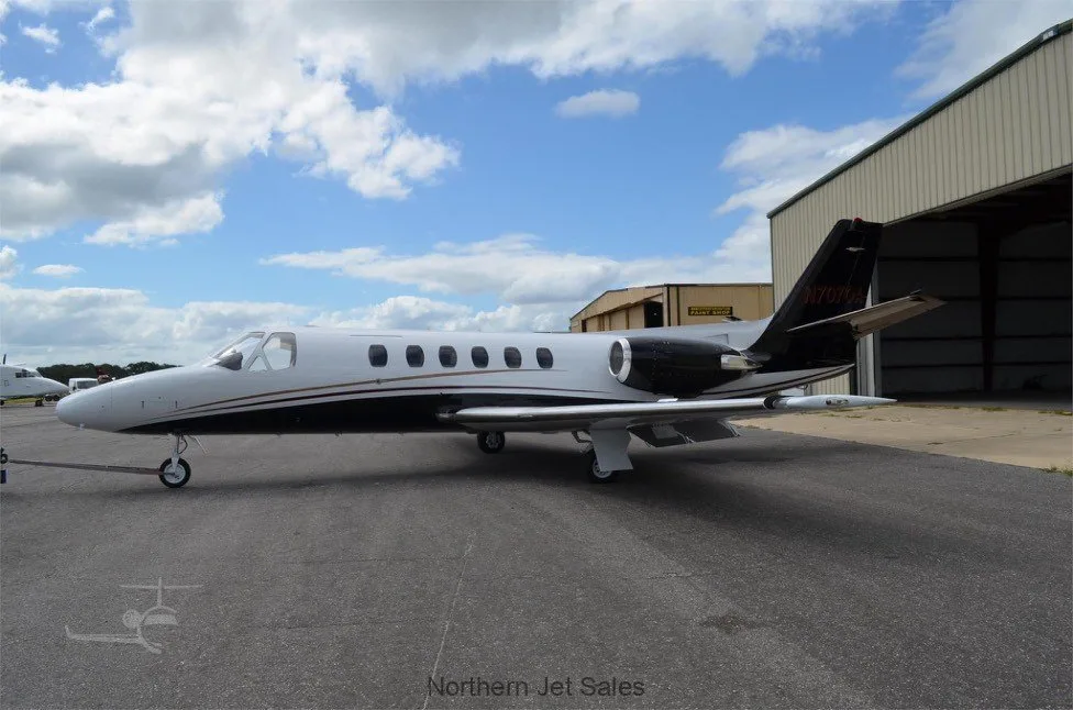Side view of a white and black jet parked on the tarmac in front of a hangar.