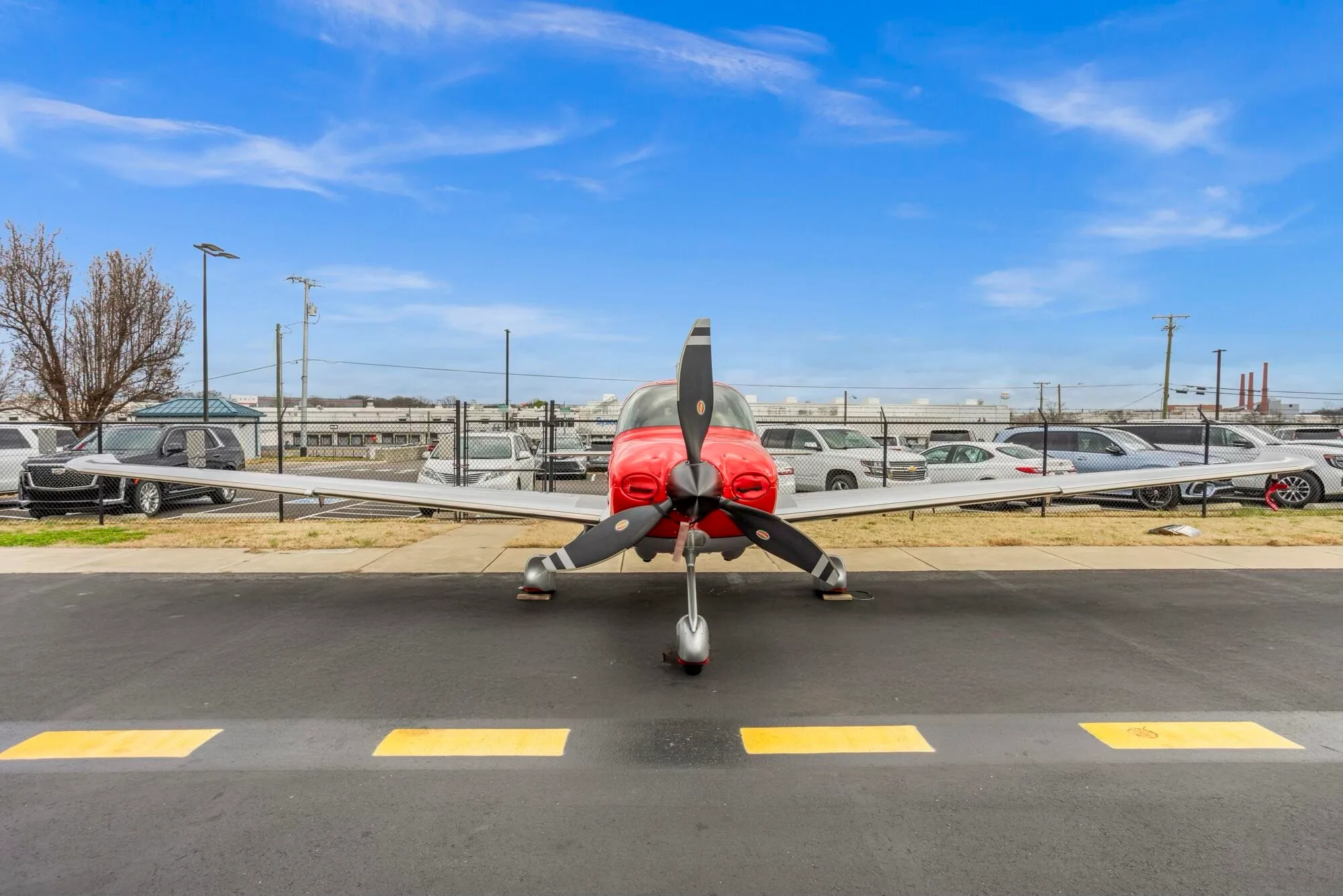 A head-on view of a red and silver Cirrus SR22 aircraft parked on an airport tarmac.