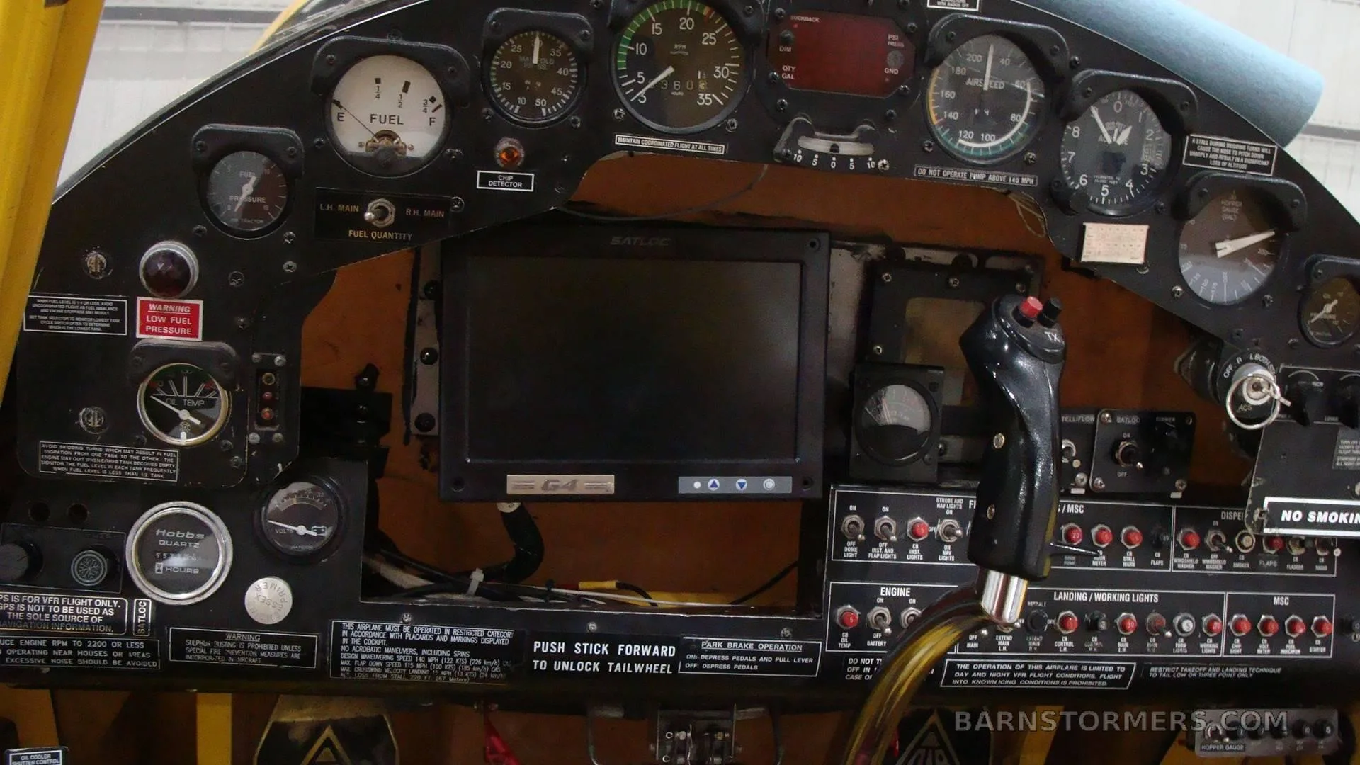 The cockpit instrument panel of the yellow agricultural aircraft, showing gauges, a display, and controls.