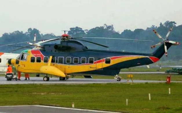 A large, dark blue and yellow helicopter with red accents is parked on a tarmac with people near its front.