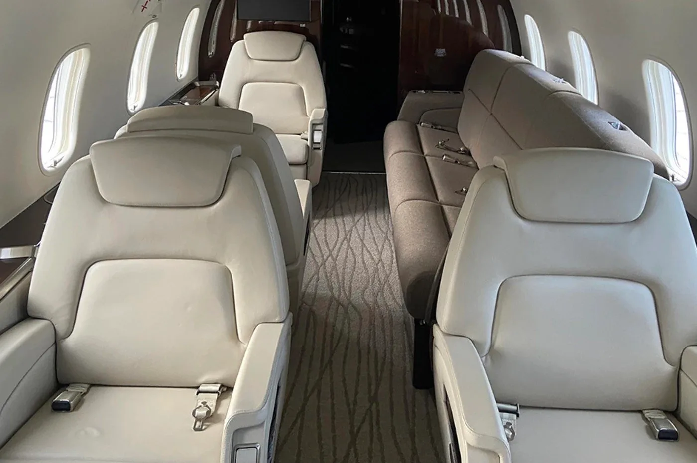 The luxurious interior cabin of a private jet, showing beige leather seats and a brown fabric sofa with a patterned carpet.