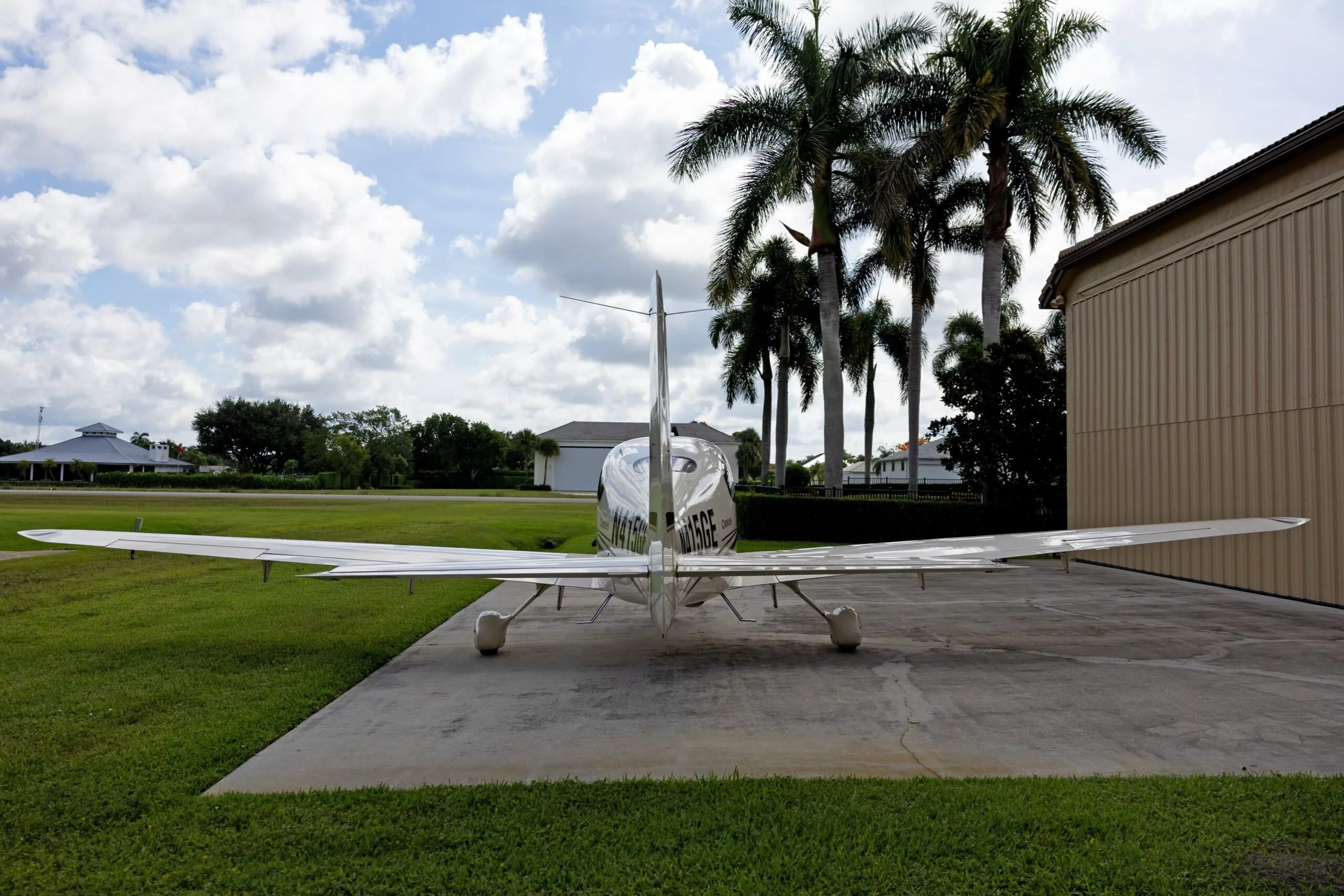 A rear view of a white Cirrus SR22 aircraft, registration N415GE, parked on a concrete pad with palm trees in the background.