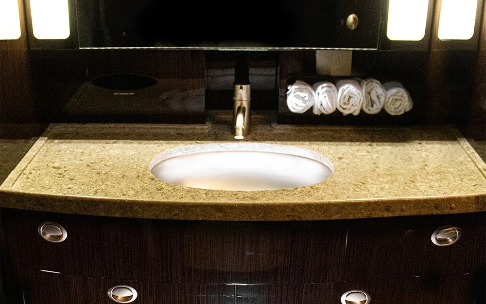 An aircraft lavatory with a modern sink, granite countertop, and rolled white towels.