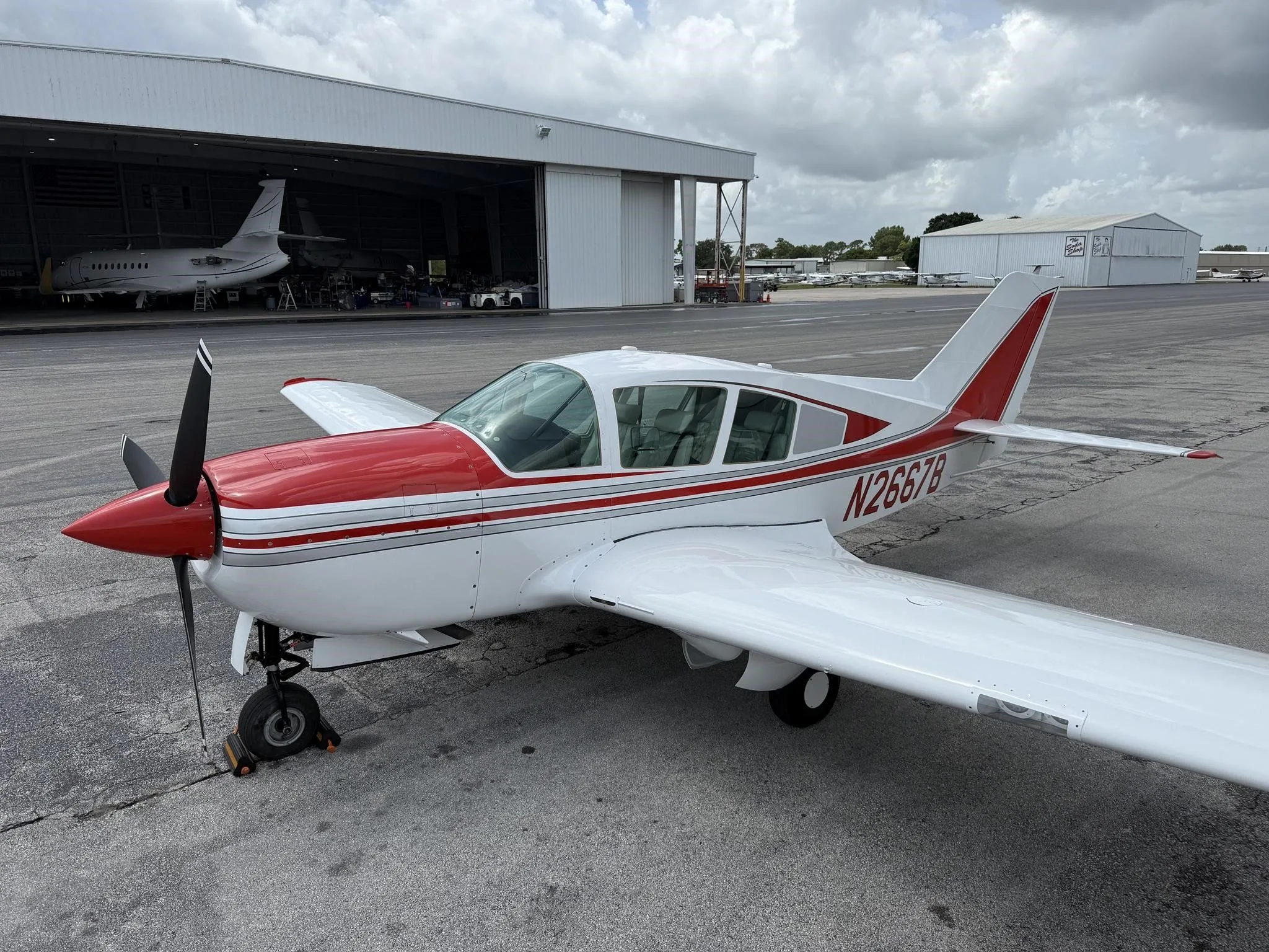 A white and red single-engine aircraft, N2667B, parked on an airport tarmac with hangars in the background.
