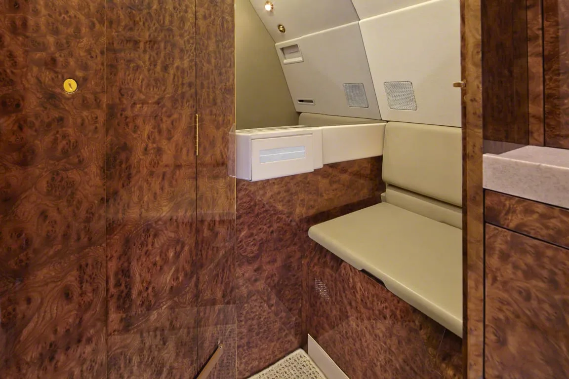 A close-up view of a private jet's interior featuring rich burl wood paneling and a beige seat or counter.