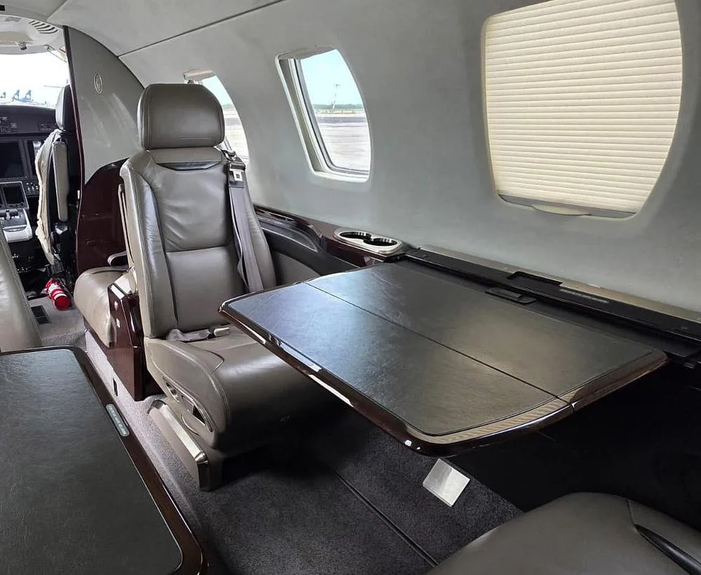 A tan leather seat and a dark wood fold-out table in the interior cabin of a private jet.