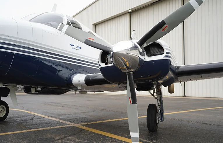 Close up of the propeller and nose of a white and blue Piper PA-34 Seneca aircraft.