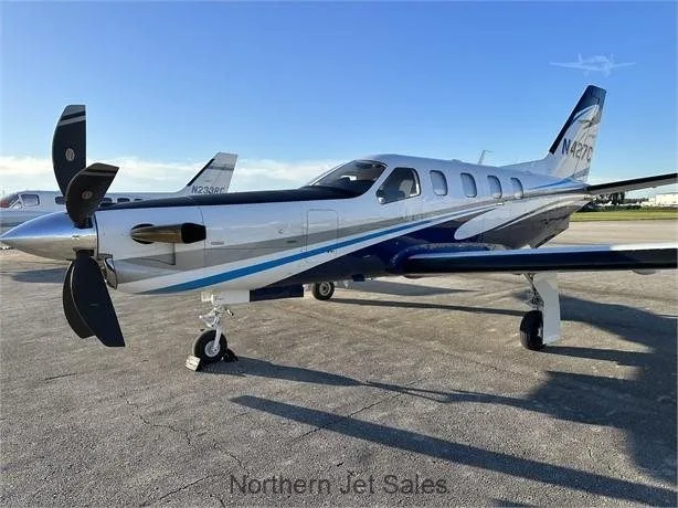 A silver and blue TBM 900 aircraft, registration N427C, is parked on the tarmac.