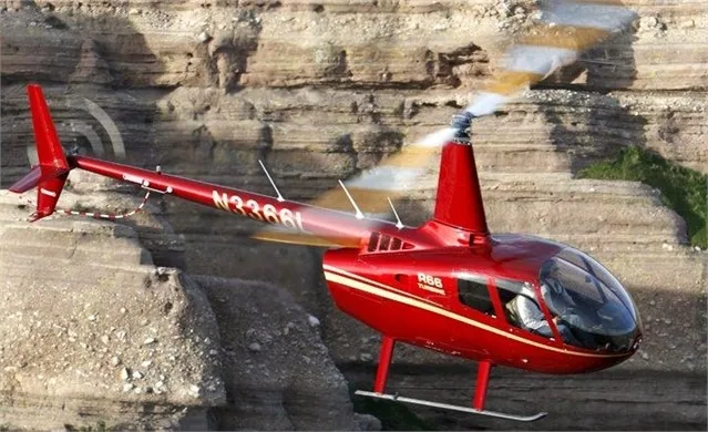 A red Robinson R66 helicopter flying near a canyon.