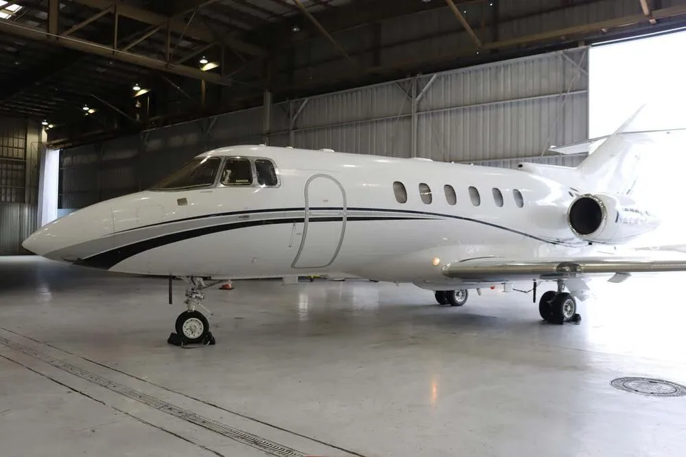 A white business jet with black and grey stripes parked in a hangar, viewed from the front-left.