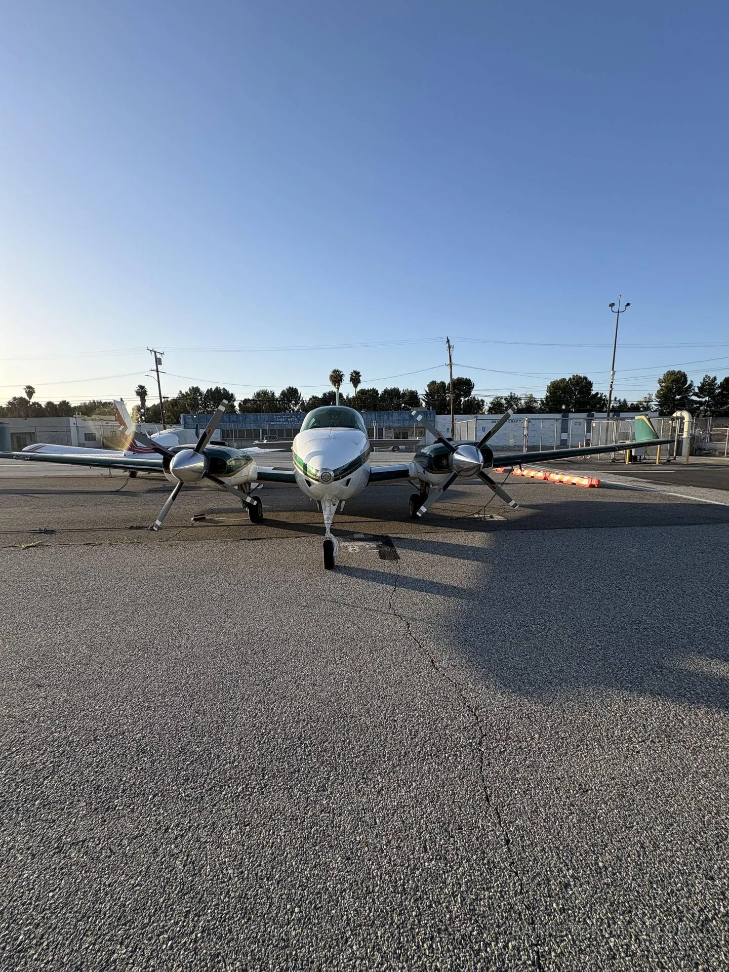 A white and green twin-engine propeller aircraft (N677Z) viewed head-on, parked on an asphalt ramp.