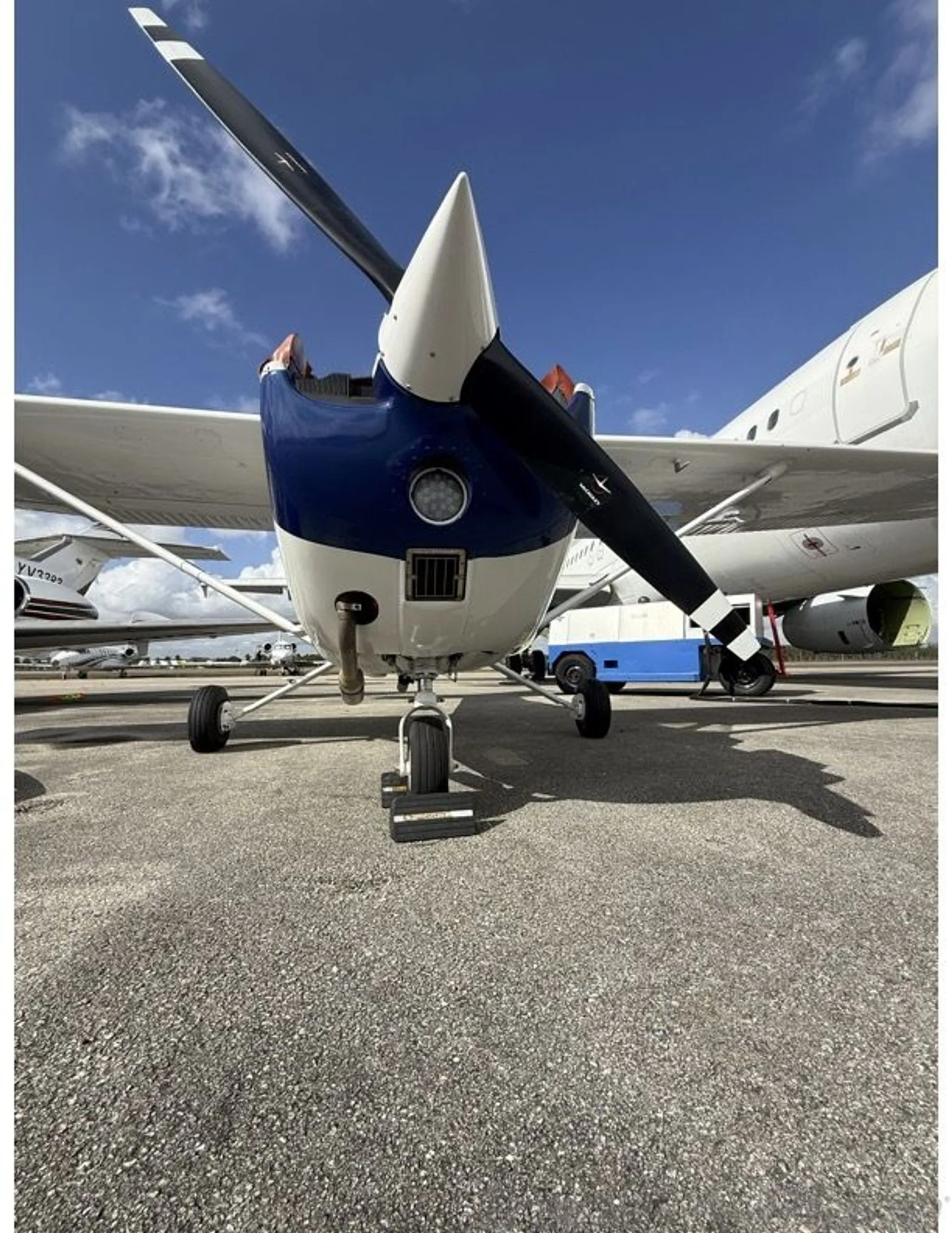 Front view of a white and blue Cessna 172 (N8180M) with its propeller, parked on an airfield.