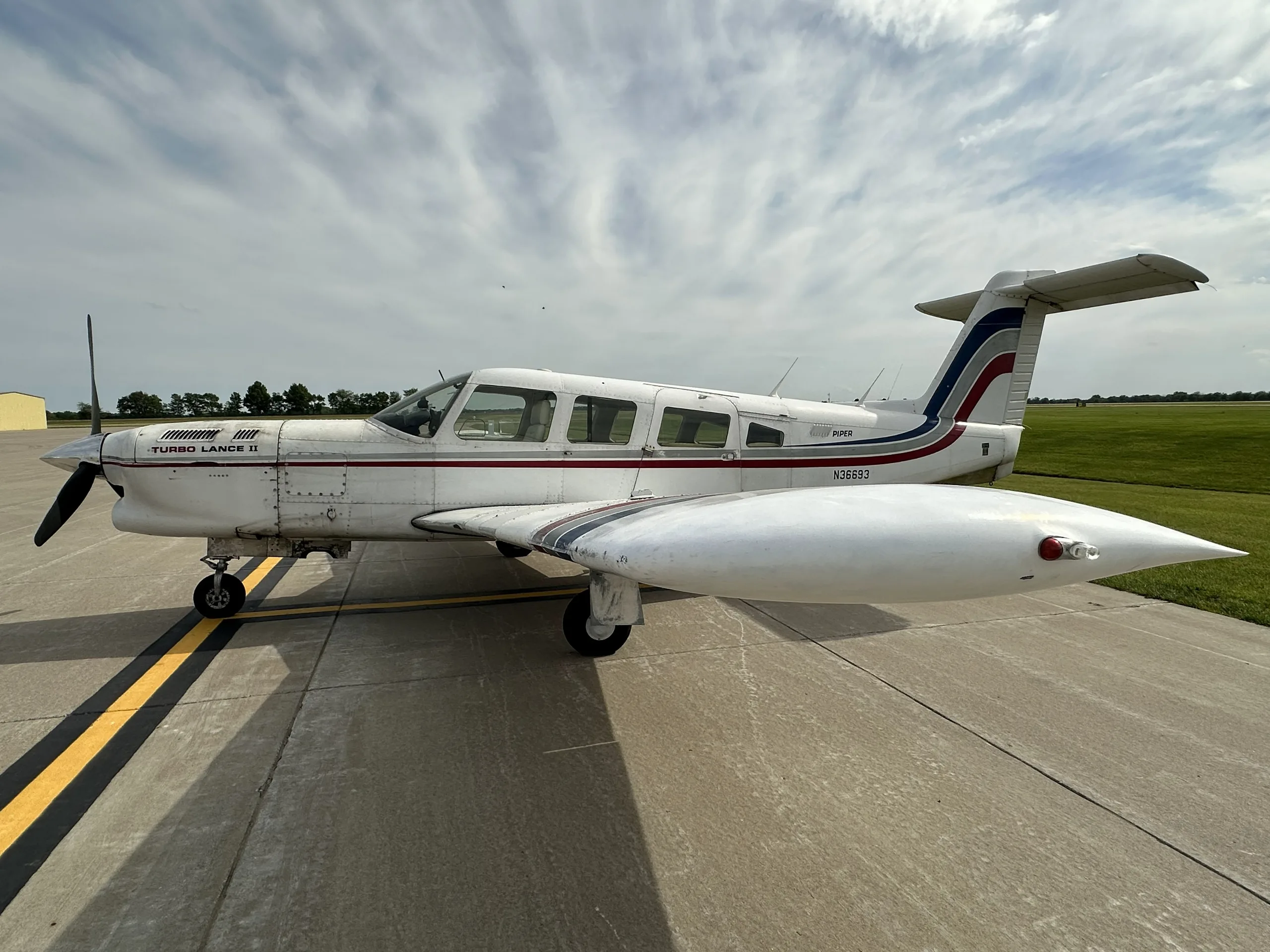 A white Piper Turbo Lance II aircraft, registration N36693, with red and blue stripes, parked on an airfield.