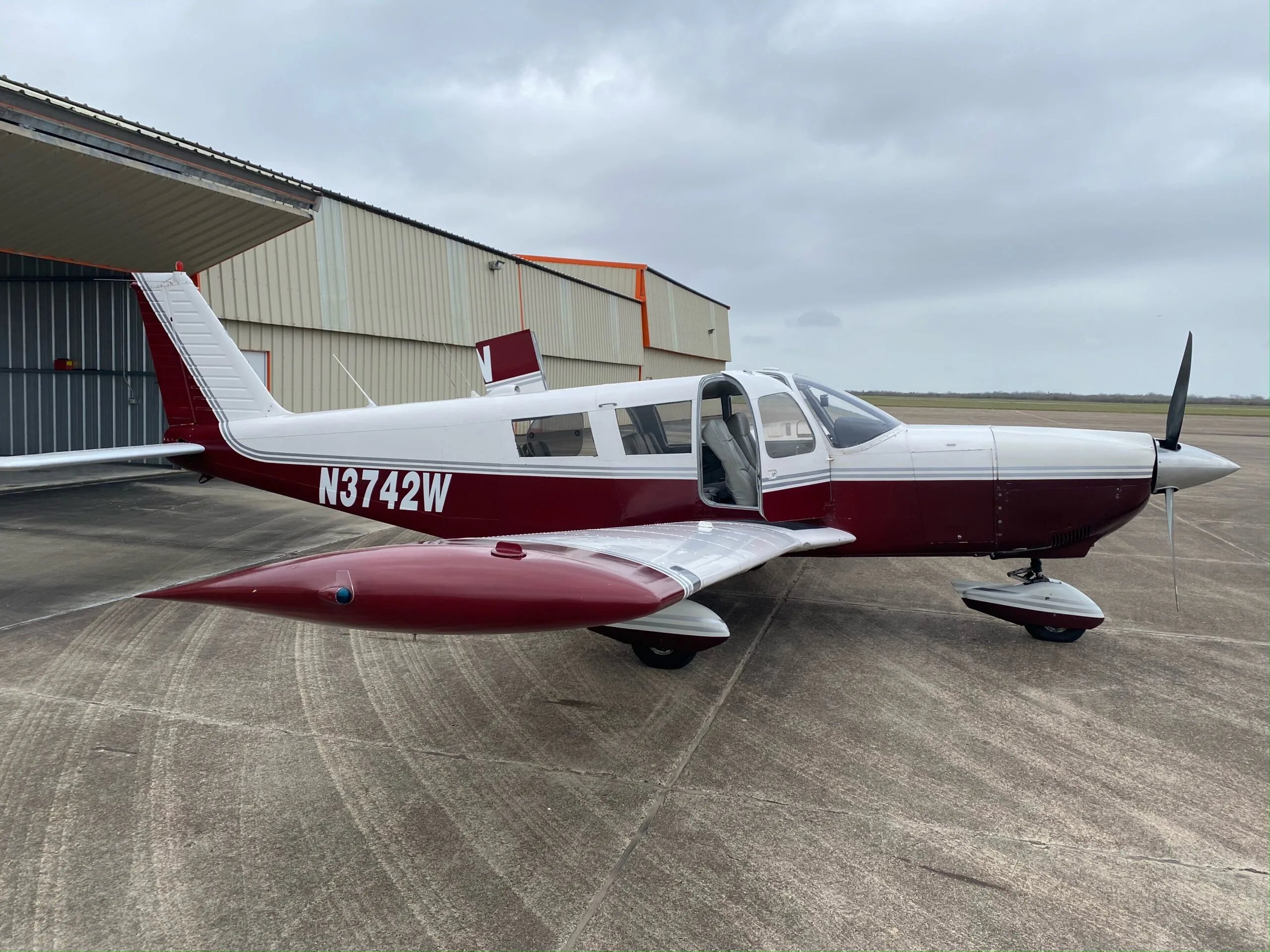 A white and maroon Piper Cherokee-style aircraft, registration N3742W, with its door open, parked on an airfield.