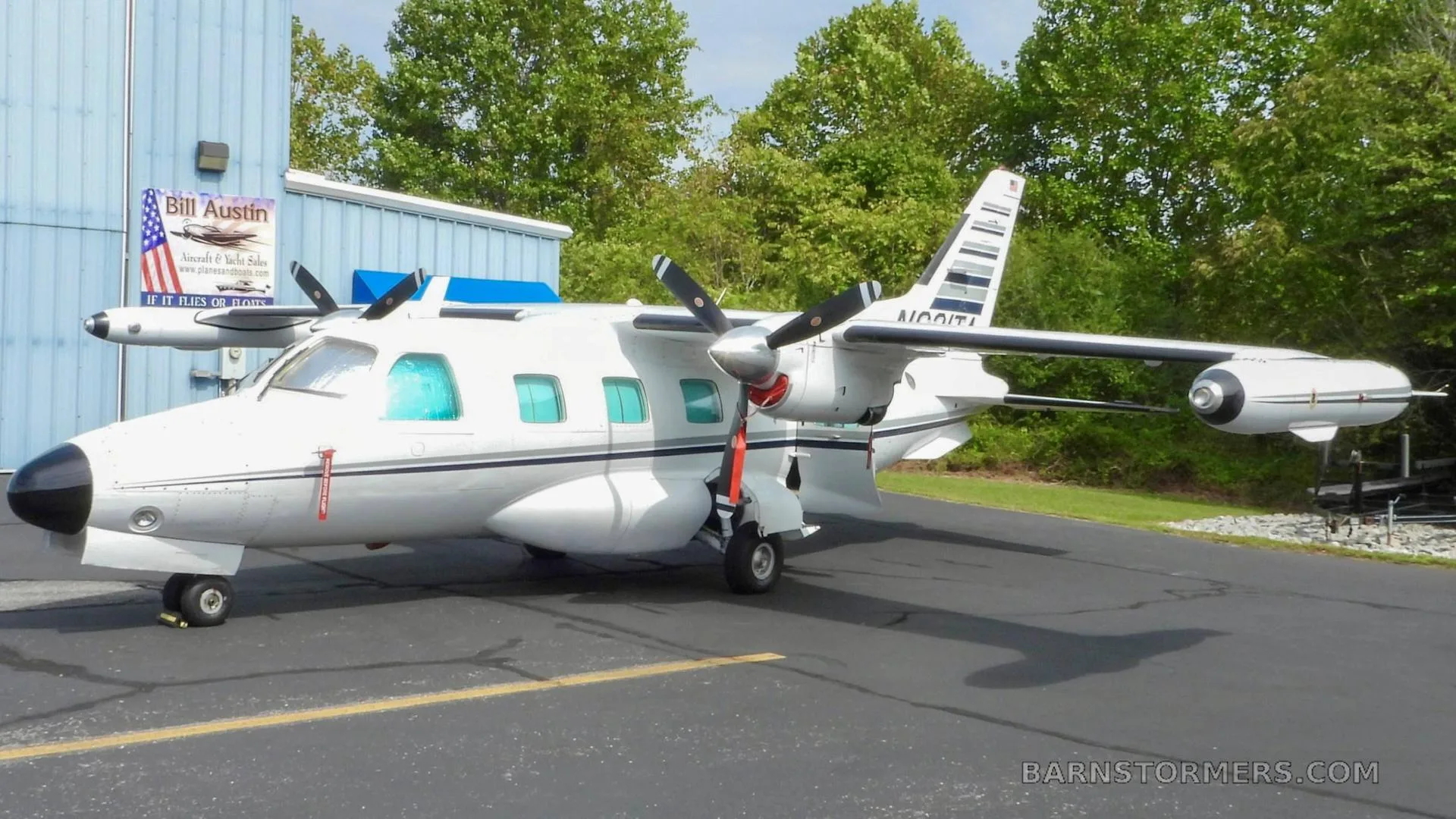 A white twin-engine turboprop aircraft, N621TA, with black accents, parked on an asphalt apron next to a blue hangar.