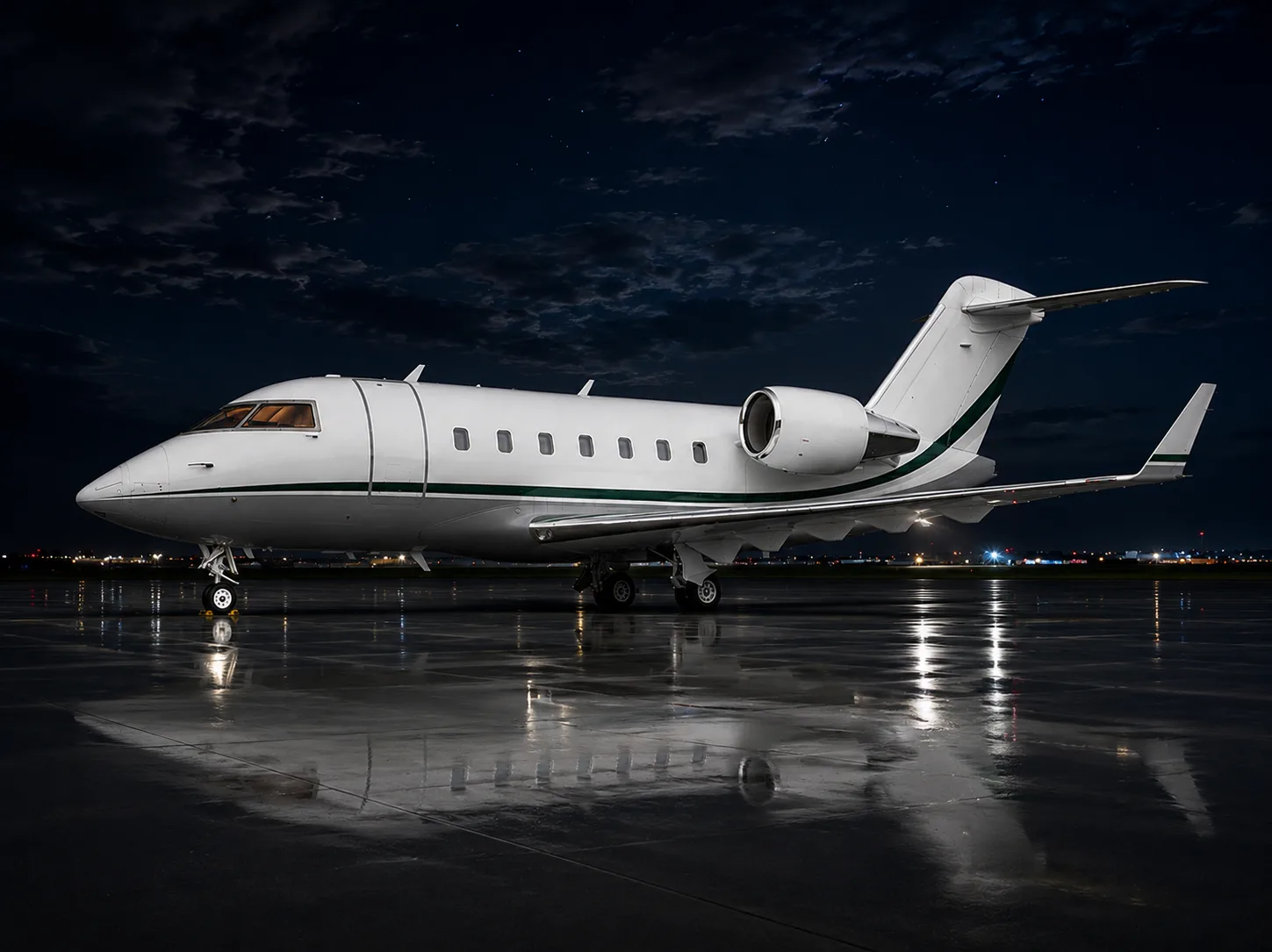 A white private jet with a green stripe sits on a wet tarmac at night, reflecting the airport lights.