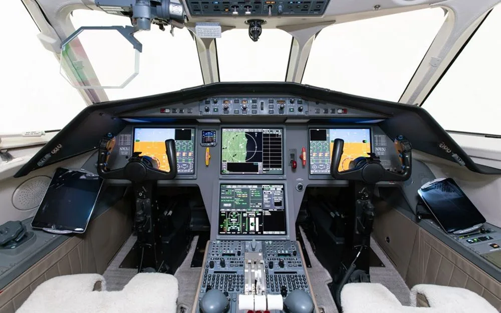 The modern cockpit of a Dassault Falcon 900EX, featuring multiple large digital displays and control yokes.