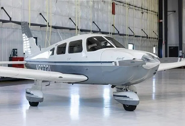 A white and grey Piper Archer III aircraft, registration N9272L, parked in a hangar, viewed from the front-right.