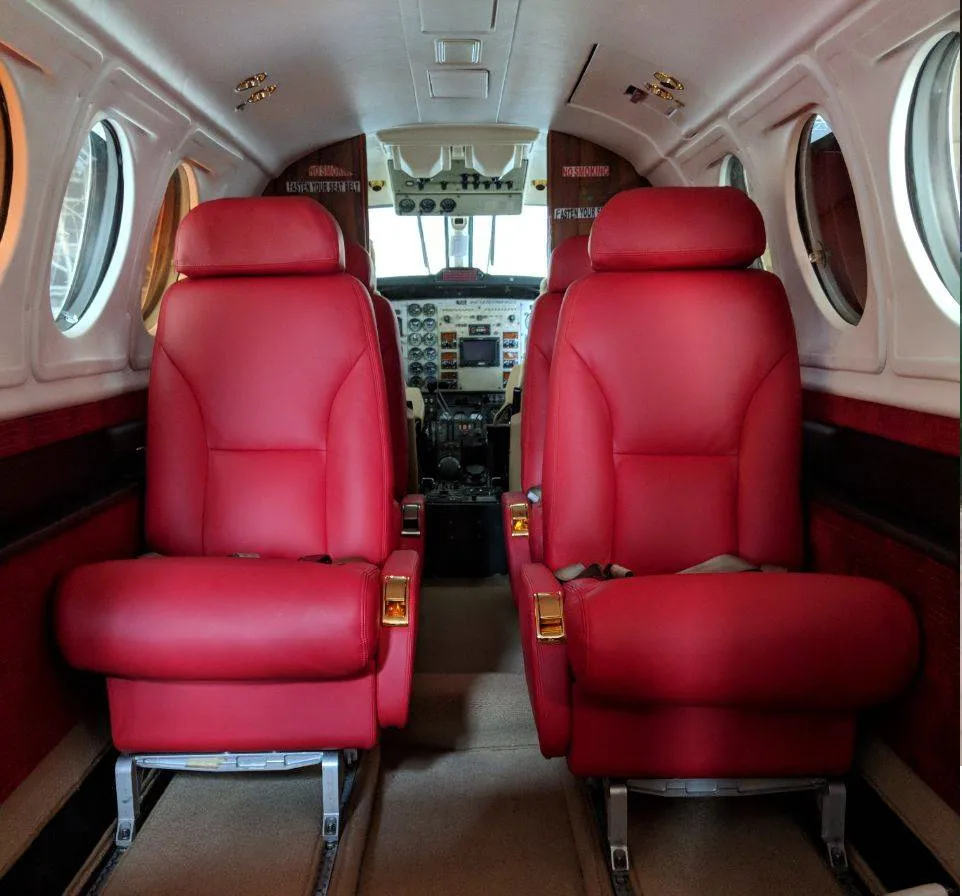 The aircraft cabin interior with two rows of red leather seats facing the cockpit.