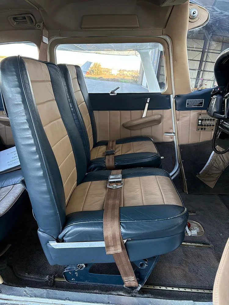 The front two-tone blue and tan leather seats of an aircraft cabin, looking towards the cockpit and outside.