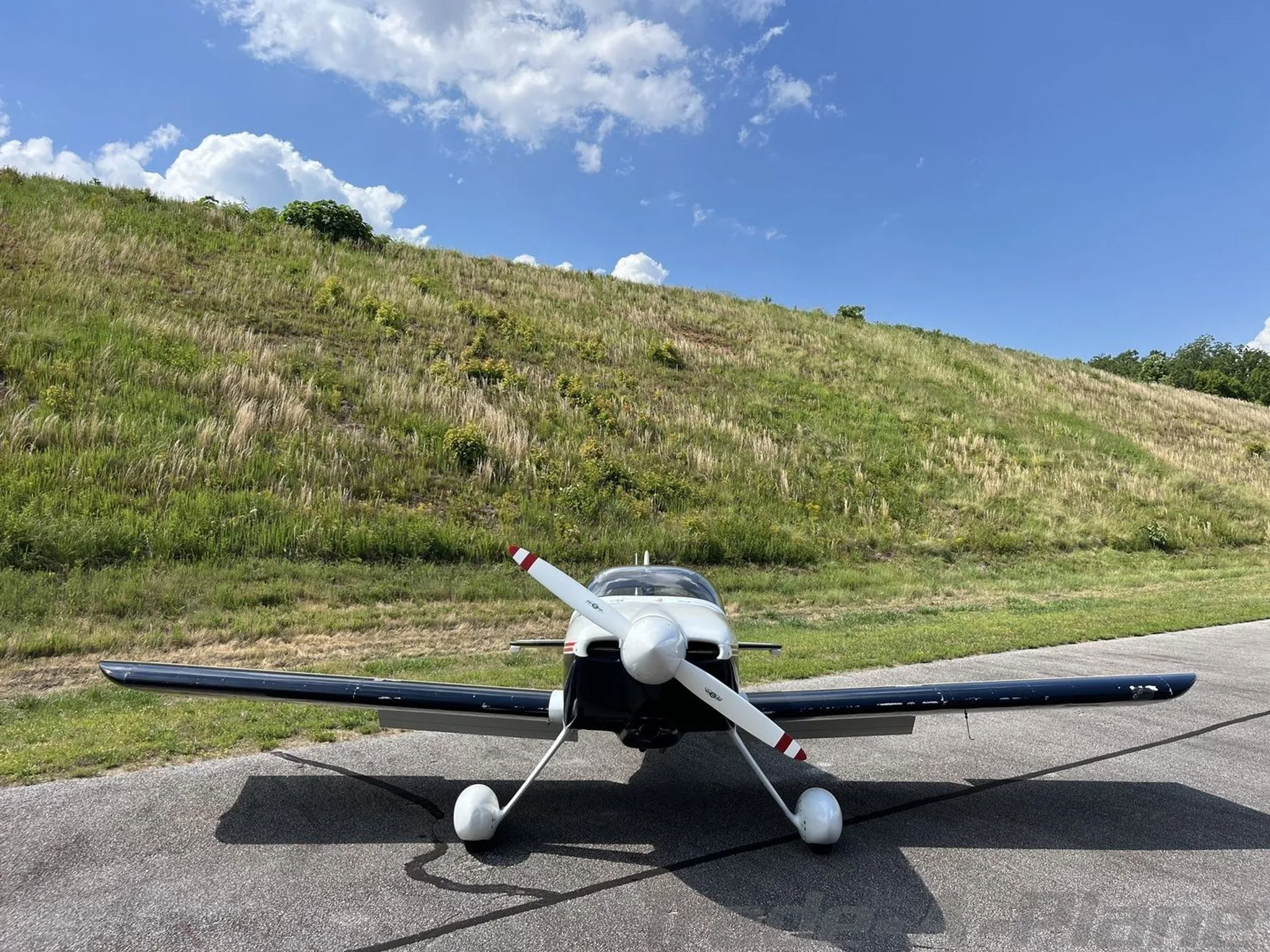 Front view of a white and dark blue single-engine aircraft with a two-bladed propeller, parked on an asphalt ramp.