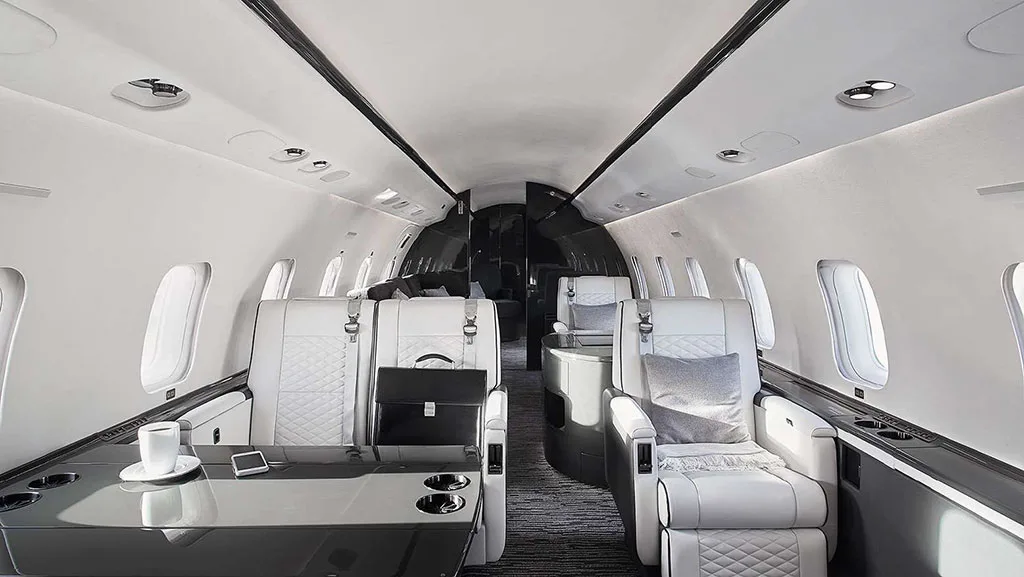 The luxurious interior cabin of a private jet, featuring white quilted leather seats, a dark table, and a black briefcase.