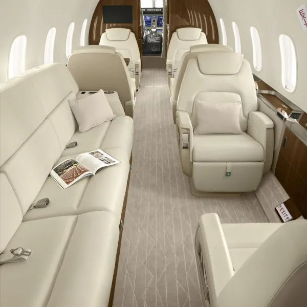 The spacious interior of a private jet featuring cream leather seating, including a sofa and individual chairs, looking towards the cockpit.