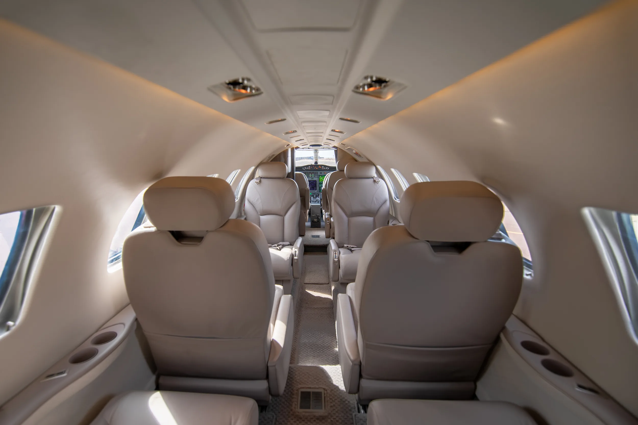 A view down the aisle of the Cessna Citation Excel cabin, showing beige leather seats and the cockpit in the distance.
