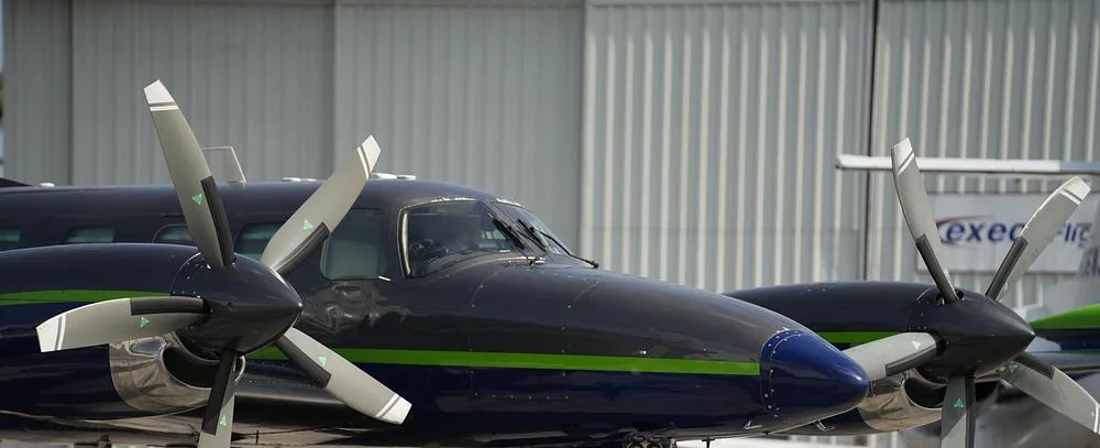 A close-up of the cockpit and propellers of a dark blue and grey twin-engine turboprop aircraft.