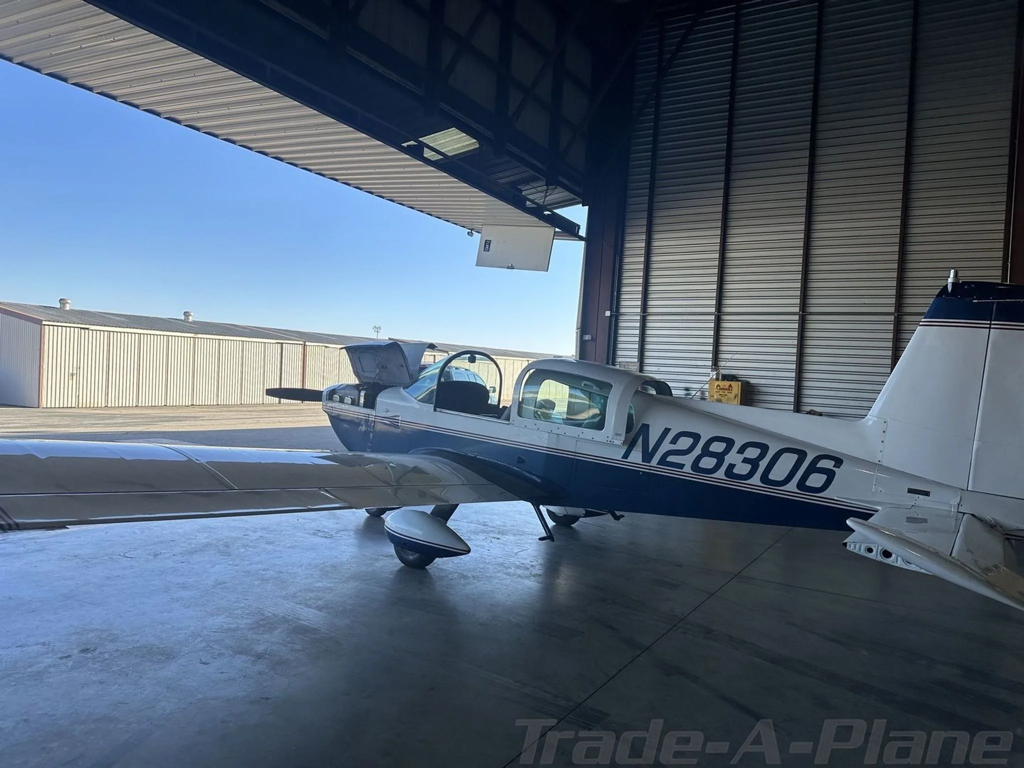 A blue and white Grumman AA5B Tiger aircraft, N28306, parked inside a hangar with the door open.