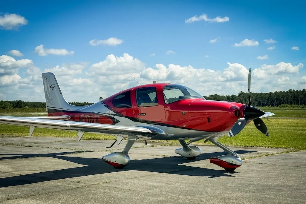 A red and silver Cirrus SR22 GTS aircraft parked on a tarmac under a blue sky.