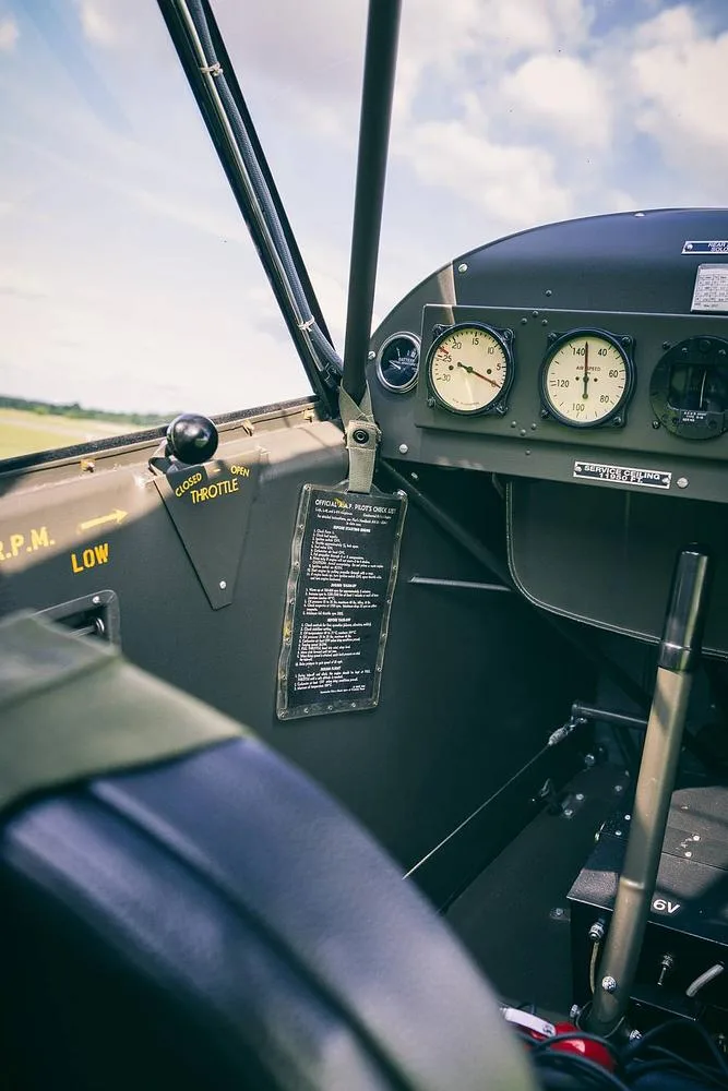 A view inside the cockpit of a vintage aircraft, showing the instrument panel with gauges, throttle control, and a checklist.